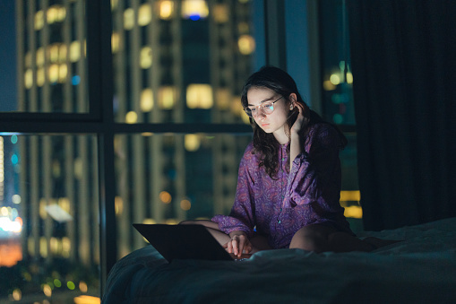 Young Caucasian woman in eyeglasses working at night in megapolis
