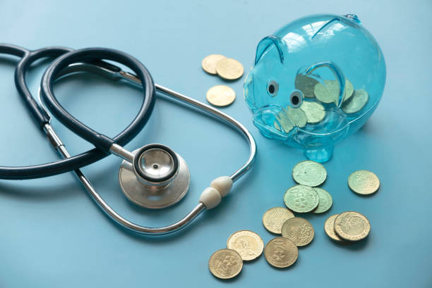Concept of saving for Medical insurance costs or expense and financial checkup. Transparent piggy bank, coins and stethoscope on blue background. stock photo