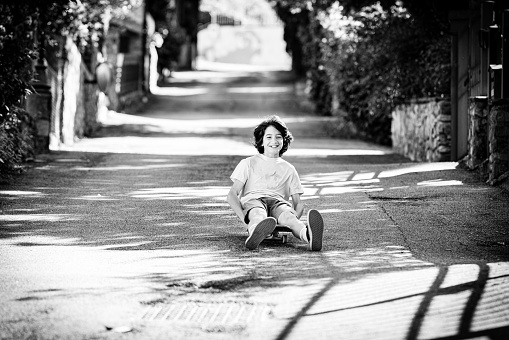 Italian boy sitting on his skateboard and skating down a steep road in a Tuscan village
