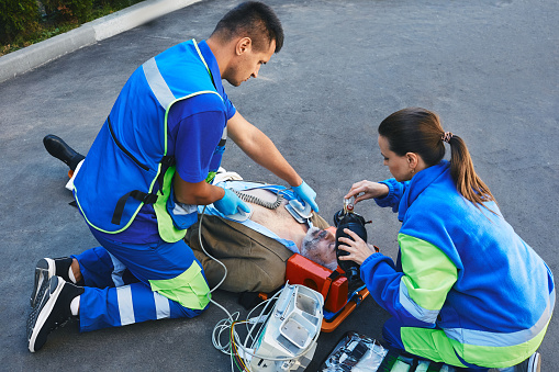Team of paramedics performing CPR with mobile defibrillator and preparing manual resuscitator for victim patient. First aid and CPR by rescue workers