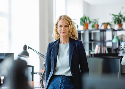 Portrait of a confident mature businesswoman standing by a desk in office. Female professional in formalwear looking at camera.