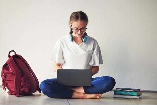 Education, laptop and woman with books on a floor for research, examination and preparation, happy and motivation. Student, girl and online university assignment, book and literature study project