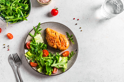 Chicken Salad with fresh vegetables and greens on white table. Roasted Chicken Fillet, green lettuce, arugula, tomatoes salad for healthy lunch, top view, copy space.