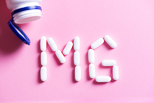 Mineral pill capsule Magnesium. White vitamin pills forming shape to Mg sign and plastic bottle on pink background, copy space, top view.