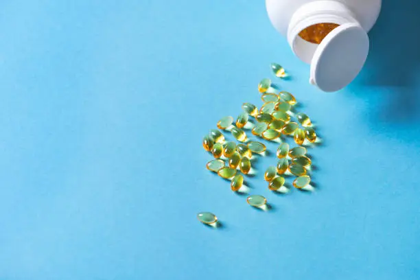 Oil filled capsules (softgel) of food supplements: fish oil, omega 3, omega 6, omega 9, vitamin A, vitamin D3, vitamin E, evening primrose oil, borage oil. Yellow softgels on blue, top view, copy space.