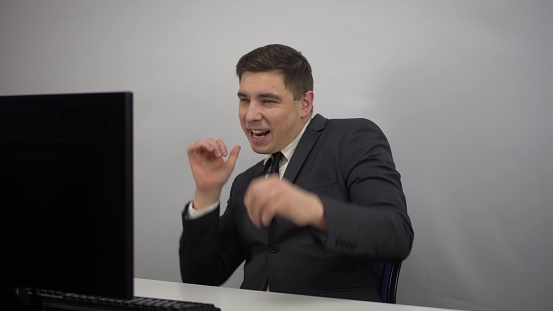Young businessman dancing after work done. A man in a suit rejoices and dances while sitting in the office. 4k