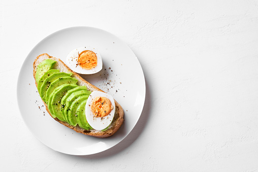 Avocado toast with hard boiled eggs on white background, copy space. Toasted bread with avocado and egg for healthy breakfast.