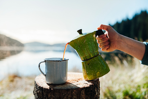 Shot of woman pouring fresh coffee on a beautiful morning on a camping vacation.
