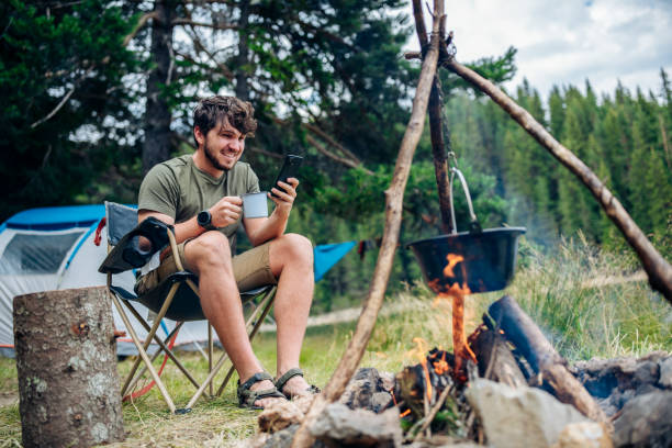 istock Man relaxing next to campfire and using phone on camping vacation. 1457407242