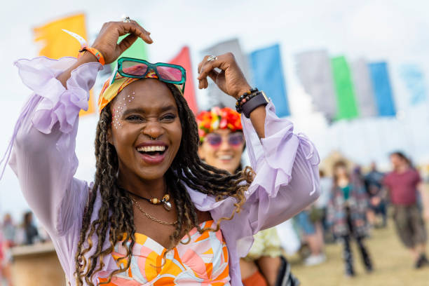 Festival Moment A shot of a young woman captured in the moment at a festival. She is smiling with excitement and joy. She is wearing vibrant clothing with sunglasses and a bandana. music festival stock pictures, royalty-free photos & images