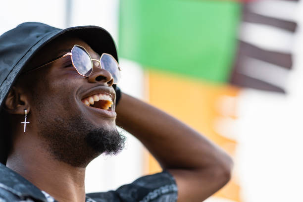 Shot of s young man at a festival in Northumberland in the north east of England. He is dancing and singing to the live music and is smiling with joy and showing happy emotions. He is wearing a bucket hat and sunglasses. There is a flag flying in the background behind him.