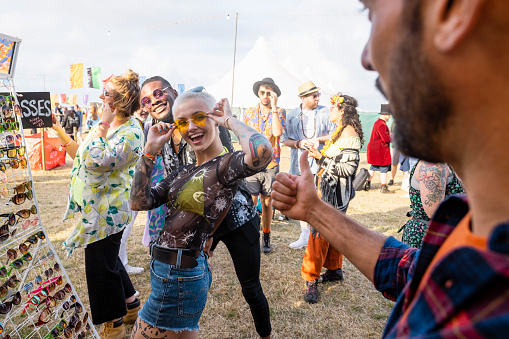 A shot of a group of friends trying on festival glasses at a festival in northumberland in the north east of England. A girl is turning towards her friend wearing the glasses.