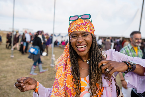 A shot of a young black woman laughing in the moment at a festival. The festival is Northumberland in the north east of England. She is wearing vibrant clothing with braided hair with a bandana and sunglasses.