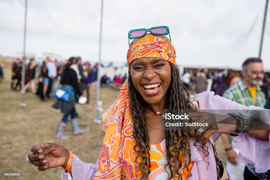 Laughter at the festival A shot of a young black woman laughing in the moment at a festival. The festival is Northumberland in the north east of England. She is wearing vibrant clothing with braided hair with a bandana and sunglasses. Music Festival Stock Photo