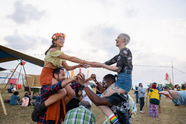 A small group of friends been playful with each other at a festival. two of the women are on their friends shoulders. They are holding hands and interacting together.