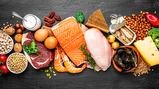 Overhead view of a large group of food with high content of healthy proteins arranged side by side on black background making a banner. The composition includes salmon beef fillet, chicken breast, eggs, yogurt, mussels, chick peas, pistachios, cheese, brown lentild, beans, shrimps, canned tuna, pumpkin seeds, soybeans among others. High resolution 42Mp studio digital capture taken with SONY A7rII and Zeiss Batis 40mm F2.0 CF lens