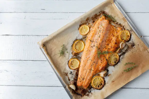 Delicious italian fish dish with oven baked or roasted half salmon fillet. Marinated with thyme, garlic and lemon. Served isolated, hot and ready to eat on a baking tray. Side view, closeup, flat lay with copy space