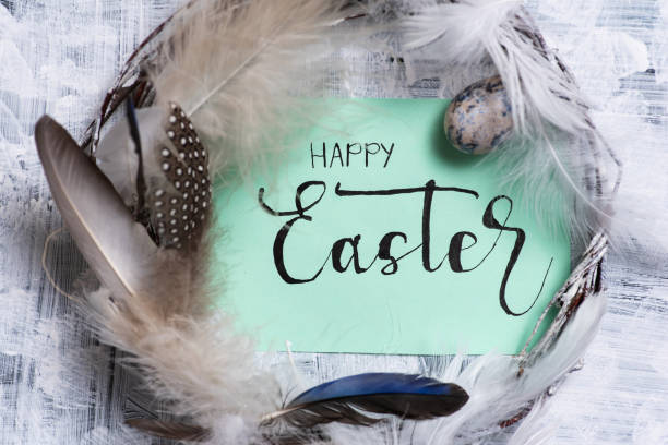 The inscription Happy Easter in a wreath of dry branches decorated with colorful natural feathers on a white background