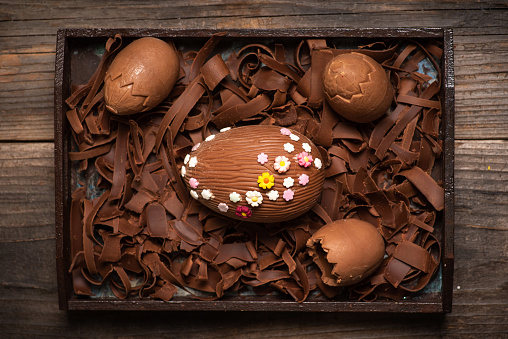 Easter decoration. Chocolate egg decorated with small multi-colored flowers on a chocolate background