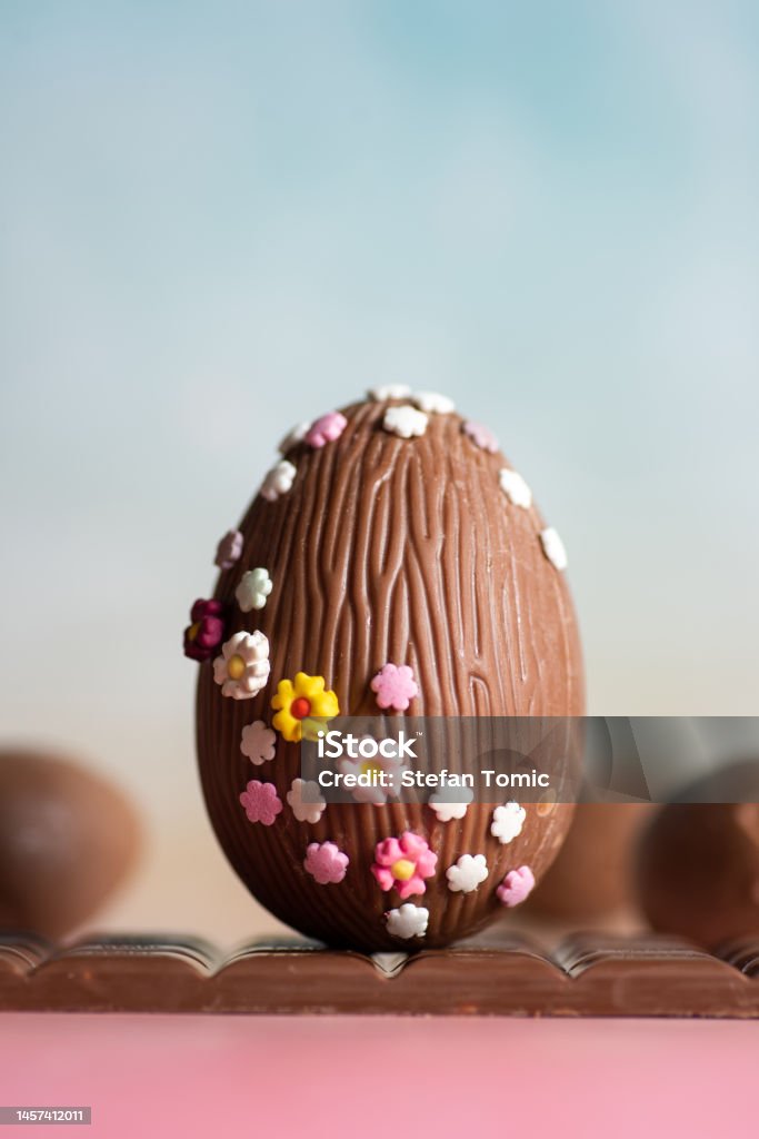 Easter decoration. Chocolate egg decorated with small multicolored flowers Easter decoration. Chocolate egg decorated with small multicolored flowers on a pastel blue background. Easter Egg Stock Photo