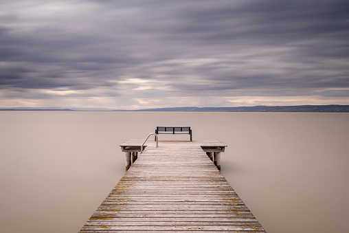 Ein alter Holzsteg mit einer Sitzbank und stillen Wasser bei schöner Fernsicht