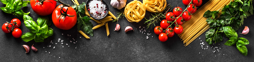 Uncooked pasta and vegetables cooking food background, banner. Various italian pasta, tomatoes, fresh basil herbs and spices, italian cuisine concept.