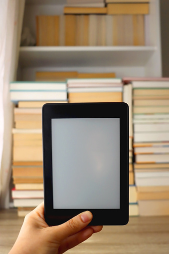 Digital tablet with stacked books in library close up