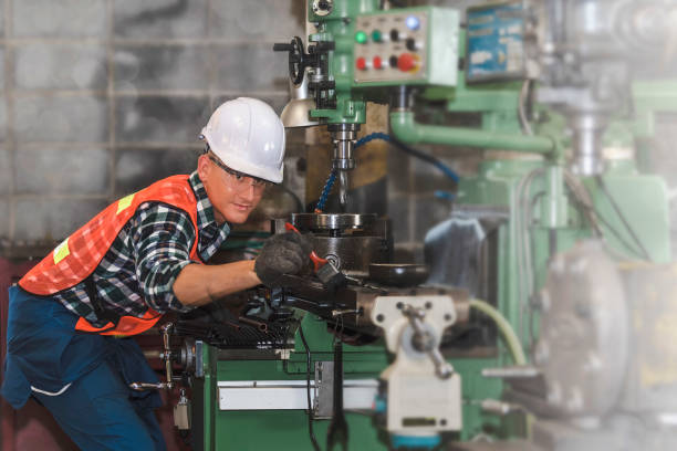 Engineer working on a metal lathe machine in a factory background that is blurry stock photo