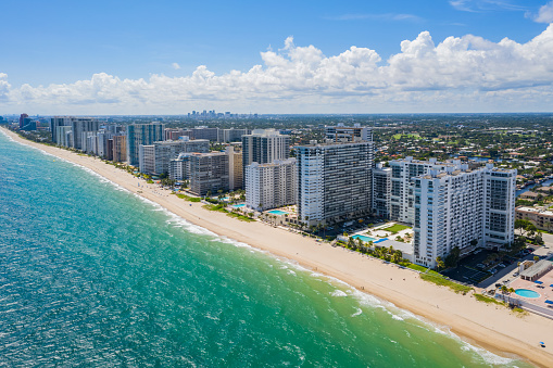 Aerial drone view of the coastline of the Galt Mile neighborhood, in Fort Lauderdale, beach with modern buildings, towers, palms, turquoise sea, blue sky
