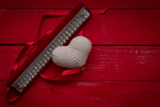 Red wooden heart on a notepad and a yellow pencil on a wooden table