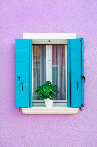 Lavender painted facade of the house and window with blue shutters. Colorful architecture in Burano island, Venice, Italy.
