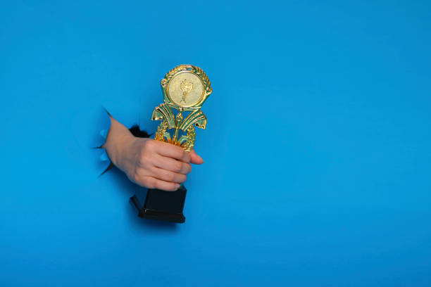 image of trophy in hand, concept for winning or success. Golden trophy on blue background, top view with space for text stock photo