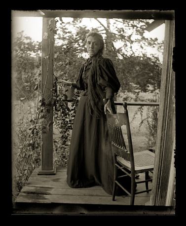 Beautiful Black and White portrait of an American Farmer woman wearing Victorian-era clothing. Taken on the front porch of her farmhouse dressed in her best clothes--probably on a Sunday afternoon. The image was digitally restored from a glass plate taken circa 1890.