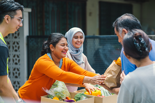 A smiling female volunteer and her colleague distributing grocery food at community food bank
