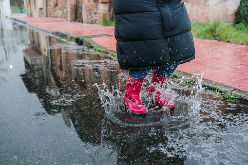 Woman with boots splashing on a puddle on a rainy day