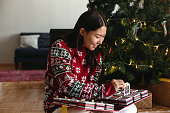 リビングルームのクリスマスツリーの近くに座ってアドベントカレンダーを開くアジアの若い女性