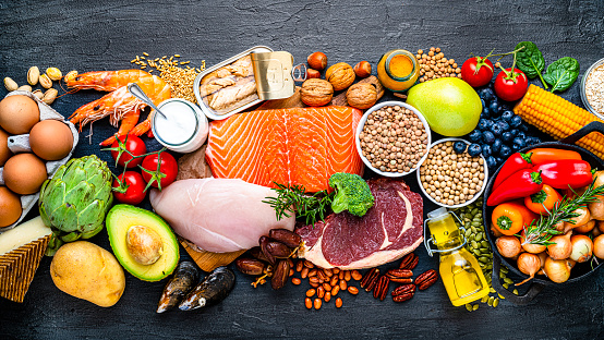 Overhead view of a large group of healthy raw food for flexitarian mediterranean diet arranged side by side on dark background. The composition includes salmon, chicken breast, canned tuna, cow steak,  fruits, vegetables, nuts, seeds, dairi products, olive oil, eggs and legumes. High resolution 42Mp studio digital capture taken with SONY A7rII and Zeiss Batis 40mm F2.0 CF lens