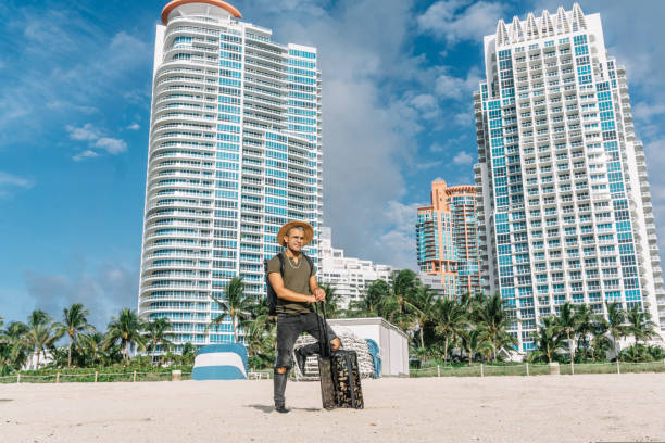 Hipster man with luggage bag on wheels standing on the south beach in miami. stock photo