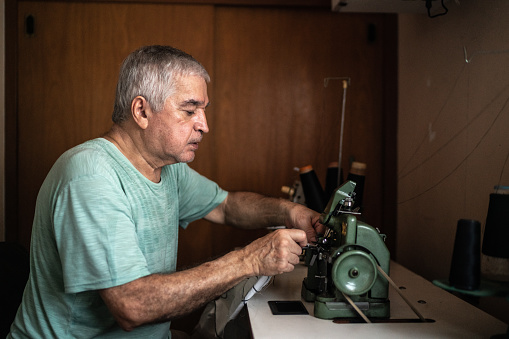 Senior man using a sewing machine at home