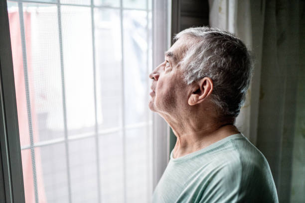 istock Senior man contemplating looking through window at home 1457437210