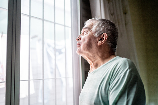 Senior man contemplating looking through window at home