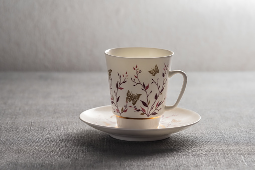 Close-up of a single empty bone China footed tea cup and saucer with a flower pattern, made in England, from directly above standing on a wooden table