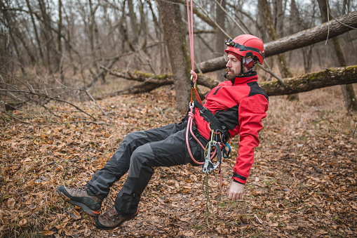A millennial mountain rescuer uses a rope to descend a steep terrain in the forest