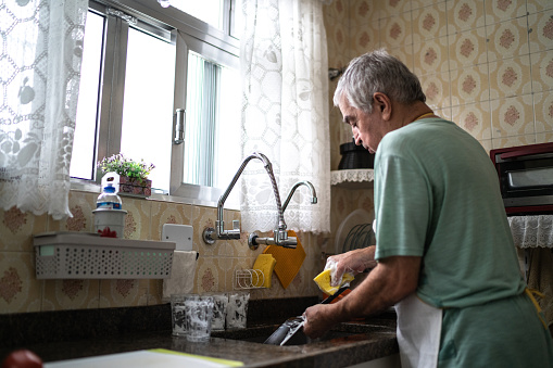Senior man washing dishes in kitchen sink at home