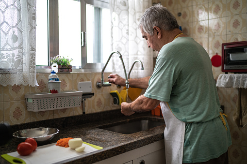 Senior man washing hands in the kitchen sink at home