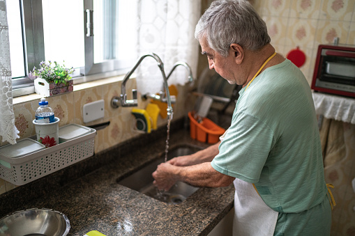 Senior man washing hands in the kitchen sink at home
