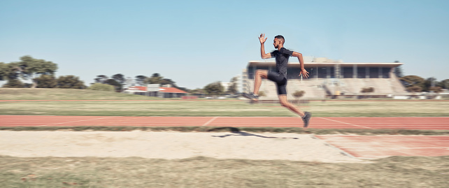 Long jump, athletics and fitness with a sports man jumping into a sand pit during a competition event. Health, exercise and training with a male athlete training for competitive track and field