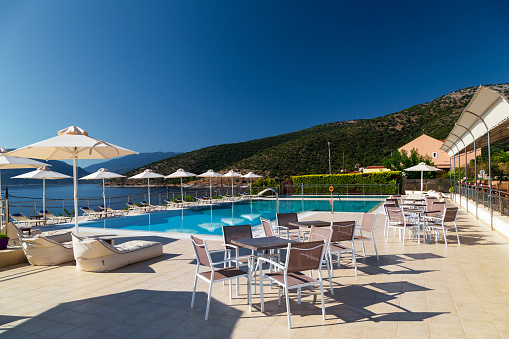 Luxury swimming pool with empty deck chairs, tables and umbrellas at the resort with beautiful sea view. Greek island.