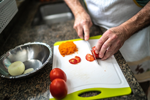 Close-up of a man cutting tomato in a cutting board in the kitchen at home