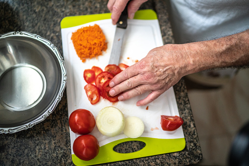 Close-up of a man cutting tomato in a cutting board in the kitchen at home